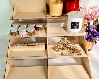 May include: A wooden tiered display stand with clear acrylic shelves. The stand is decorated with a wooden sign that reads "OAK CRAFT & CO". The stand is filled with various items, including candles, jars, and dried flowers.