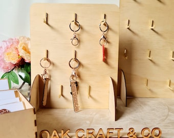 May include: Wooden key rack with gold hooks and a sign that reads "OAK CRAFT & CO". The rack has several keychains hanging from it, including a red keychain with a wooden charm that says "EVERWOODLAB".