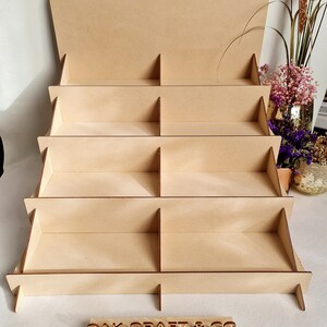 May include: A wooden display stand with five shelves and eight compartments. The stand is made of natural wood and has a rustic look. The stand is labeled "OAKCRAFT & CO."