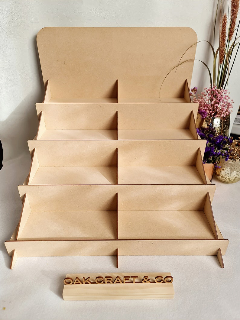 May include: A wooden display stand with five shelves and eight compartments. The stand is made of natural wood and has a rustic look. The stand is labeled "OAKCRAFT & CO."