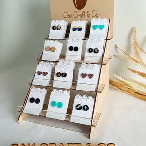 May include: A wooden display stand with multiple shelves showcasing a variety of colourful polymer clay earrings. The earrings are displayed on small white cards. The stand has a sign that reads "Oak Craft & Co."
