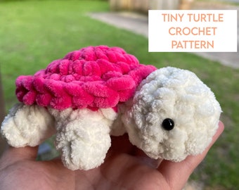 May include: A crocheted turtle toy with a pink shell and white body. The turtle has black eyes and is made with a fluffy yarn.