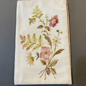 May include: A white fabric pouch with a floral embroidery design. The embroidery features pink and yellow flowers with green leaves.