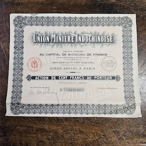 May include: A vintage stock certificate from Union Miniere Indochinoise, featuring ornate borders and text in French. The certificate states "ACTION DE CENT FRANCS AU PORTEUR" and includes the number 013,759. The document is on a textured paper.
