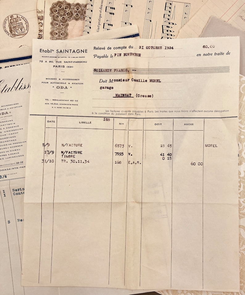 May include: A vintage invoice from Etabl' Saintagne, a company that sold car parts and accessories, dated October 31, 1934. The invoice is for a customer named Monsieur Camille Morel, who owns a garage in the town of Mailsat, Creuse, France. The invoice lists three items: N/Facture, N/Facture Timbre, and TR. 30.11.34. The total amount due is 60.00 francs.