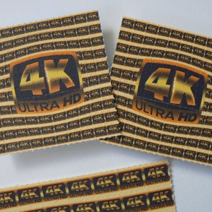 May include: Three sheets of paper with a repeating pattern of "4K ULTRA HD" printed on them. The sheets are beige with black and gold lettering.