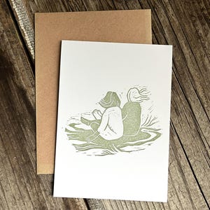 May include: A green linocut print of two figures sitting back to back on a grassy hill.