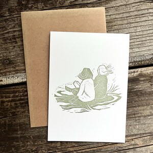 May include: A green linocut print of two people sitting back to back on a grassy surface.