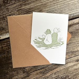 May include: A green linocut print of two people sitting back to back on a grassy hill.