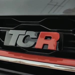 Pode incluir: Uma grelha de carro preta com um emblema "TCR" vermelho e preto.