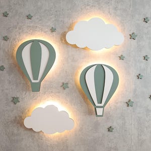 May include: A wall decor set featuring two hot air balloons and two clouds, all with a soft green and white color scheme. The balloons and clouds are illuminated with a warm glow, and small star-shaped accents are scattered around.