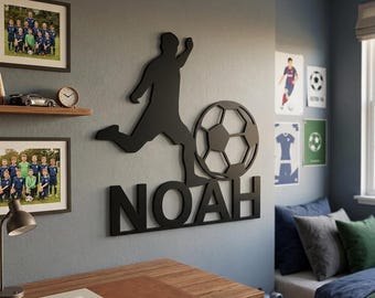 Op de afbeelding: Een zwart wandbord met een silhouet van een voetballer die tegen een bal schopt, geplaatst boven de naam NOAH in dikke hoofdletters. Het decoratieve object is bevestigd aan een grijze muur en zorgt voor een opvallend visueel contrast.
