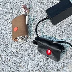 Può includere: Una disposizione piatta di vari oggetti per organizzare cavi e fili. Un laptop nero, un fermacavi in ​​pelle rosso, un fermacavi in ​​pelle marrone, un fermacavi in ​​pelle bianco e un adattatore di alimentazione nero sono su una superficie di pietra grigia.