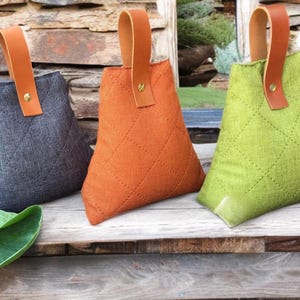 Könnte beinhalten: Drei Türstopper aus Stoff mit einem gesteppten Muster. Die Türstopper sind in Grau, Orange und Grün. Jeder Türstopper hat einen braunen Ledergriff mit einem Messingknopf.