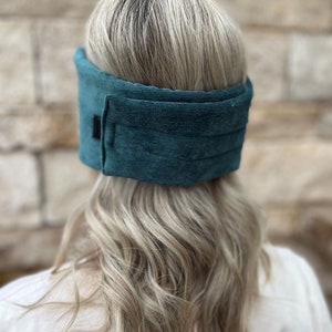 May include: Teal corduroy head wrap. The wrap is a solid teal color and has a rectangular black patch on the side. The head wrap is designed to be worn around the head.