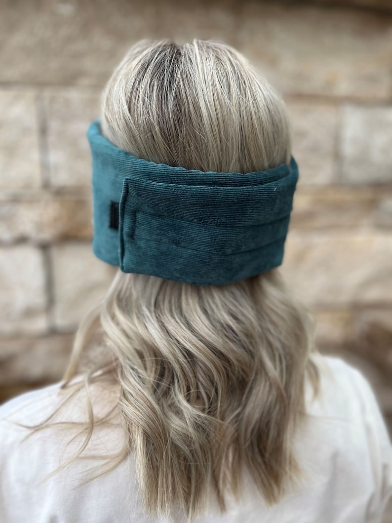 May include: Teal corduroy head wrap. The wrap is a solid teal color and has a rectangular black patch on the side. The head wrap is designed to be worn around the head.