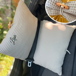 Puede incluir: Dos almohadas para reposacabezas de asiento de coche de tejido de gofre gris claro. Una almohada tiene el nombre "Lisa" bordado en escritura negra. Las almohadas tienen un forro amarillo con lunares y cierre de bot&oacute;n de madera.