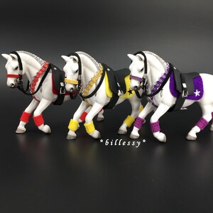 Peut inclure: Trois chevaux de jouet blancs portant des selles et des brides noires avec des accents de couleurs différentes. Le premier cheval a des accents rouges, le deuxième a des accents jaunes et le troisième a des accents violets.