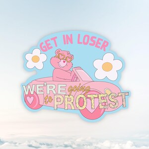Könnte beinhalten: Ein gestanzter Aufkleber mit einem rosa Bären, der herzförmige Sonnenbrillen trägt und ein rosa Cabriolet fährt. Der Text lautet GET IN LOSER WE'RE going to PROTEST. Zwei weiße Blumen mit gelben Mitten flankieren den Bären auf hellblauem Grund.