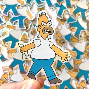May include: Holographic sticker featuring Homer Simpson from The Simpsons cartoon. Homer is depicted with a yellow complexion, white shirt, blue pants, and a brown beard, holding a bottle. The sticker has a shiny, iridescent finish.