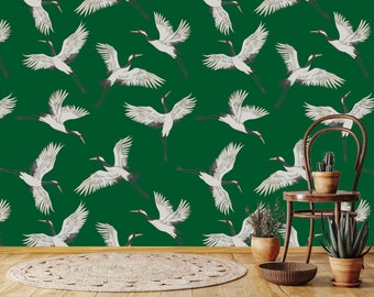 May include: A green wallpaper with a repeating pattern of white cranes. The wallpaper is shown in a room with a chair, a potted plant, and a rug.