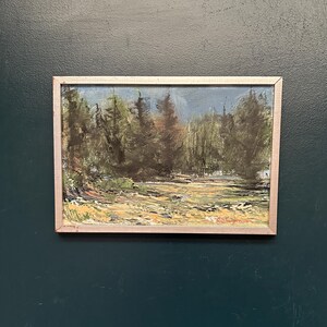 May include: A rectangular landscape painting in a light-colored frame featuring a forest scene with dark green trees, a golden-brown ground, and a blue sky. The artwork displays visible brushstrokes and includes a red signature in the bottom right corner.