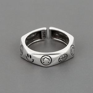 Könnte beinhalten: Ein silberner Ring mit geometrischem Design, das mehrere Smiley-Gesichter zeigt. Der Ring ist innen mit "925" gekennzeichnet.