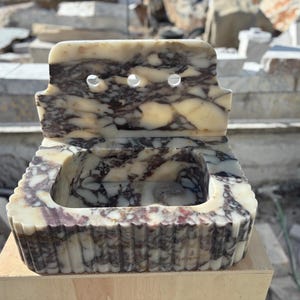 May include: A marble sink with a rectangular basin and a backsplash featuring three holes. The sink has a cream and dark purple marbled pattern. The front of the sink has a fluted design.