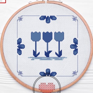 May include: A cross stitch pattern of three blue tulips in a white frame. The pattern is in a wooden embroidery hoop.