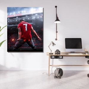 Op de afbeelding: Een professionele voetballer die een rood shirt draagt met nummer 7 en de naam "RONALDO" op de rug, viert een doelpunt in een stadion. De speler staat met zijn rug naar de camera, met de stadionverlichting en de menigte zichtbaar op de achtergrond.