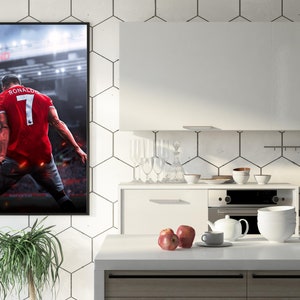 Op de afbeelding: Een ingelijste poster van een voetballer in een rood shirt met nummer 7 op de rug. De speler staat op een voetbalveld met een menigte op de achtergrond. De poster hangt aan een witte betegelde muur in een keuken.