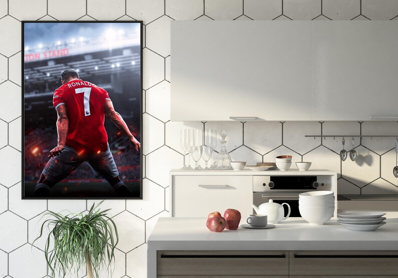 Op de afbeelding: Een ingelijste poster van een voetballer in een rood shirt met nummer 7 op de rug. De speler staat op een voetbalveld met een menigte op de achtergrond. De poster hangt aan een witte betegelde muur in een keuken.