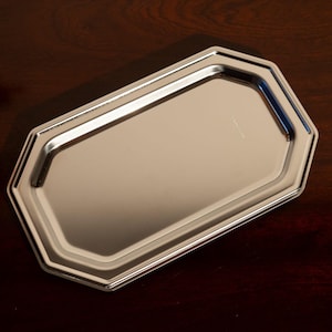 Op de afbeelding: Een zilverkleurige, achthoekige dienblad met een reflecterend oppervlak. De dienblad heeft een opstaande rand en een eenvoudig, elegant ontwerp. De dienblad is waarschijnlijk van metaal en is geschikt voor serveren of presenteren.
