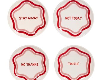 Può includere: Quattro piatti in ceramica bianca con un bordo ondulato rosso e rosa. Ogni piatto ha una frase diversa in rosso: "STAY AWAY", "NOT TODAY", "NO THANKS" e "TOUCHÉ".