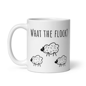 Könnte beinhalten: Weiße Keramik-Kaffeetasse mit schwarzem Umriss von drei Schafen und dem Text "WHAT THE FLOCK?"