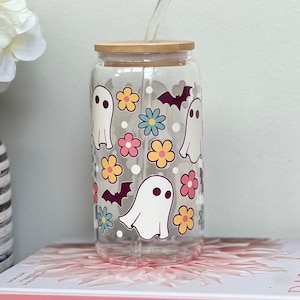 May include: A clear glass tumbler with a bamboo lid and a reusable straw. The tumbler has a Halloween-themed design with white ghosts, bats, and colorful flowers.
