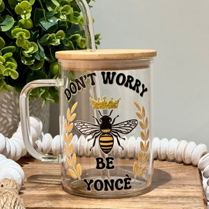 May include: A clear glass mug with a bamboo lid and a black and gold bee design. The mug has the text "Don't Worry Be Yoncé" printed on it.