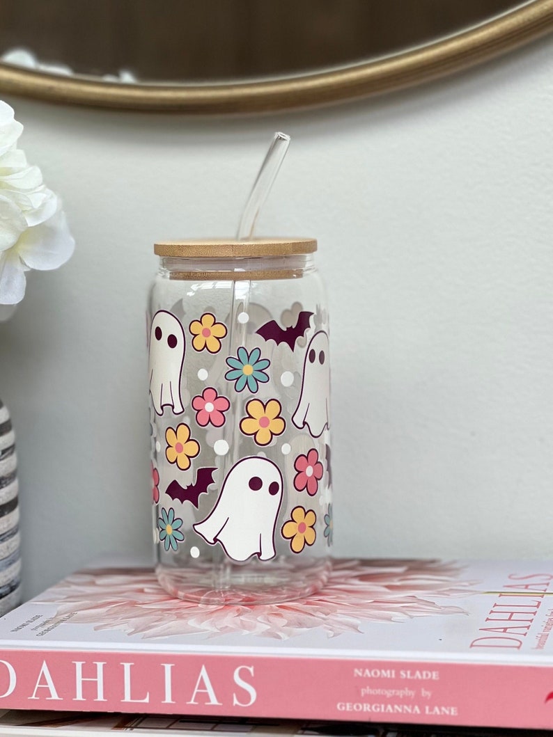 May include: A clear glass tumbler with a bamboo lid and a reusable straw. The tumbler has a Halloween-themed design with white ghosts, bats, and colorful flowers.