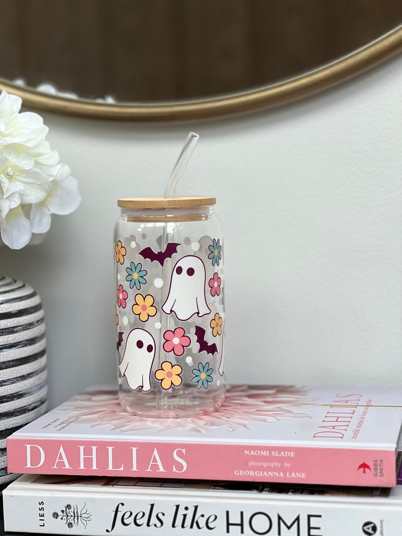 May include: A clear glass tumbler with a wooden lid and a straw. The tumbler has a Halloween-themed design with ghosts, bats, and flowers in pink, yellow, blue, and green.