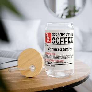 May include: A glass coffee mug with a white label that reads "Prescription Coffee" and "Vanessa Smith". The label also includes a red "Rx" symbol and instructions for use. The mug has a bamboo lid and a clear glass straw.