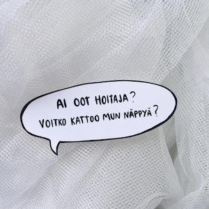 Peut inclure: Une épingle blanche en forme de bulle de dialogue avec une bordure noire et du texte en finnois. Le texte se lit "AI OOT HOITAJA? VOITKO KATTOO MUN NÄPPYÄ ?" L'épingle est posée sur un fond blanc texturé.