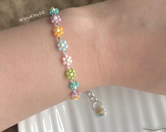 Può includere: Un set di braccialetto e orecchini con perline colorate, con piccole perline a forma di fiore in tonalità di rosa, blu, verde e giallo. Il braccialetto ha una chiusura argentata.