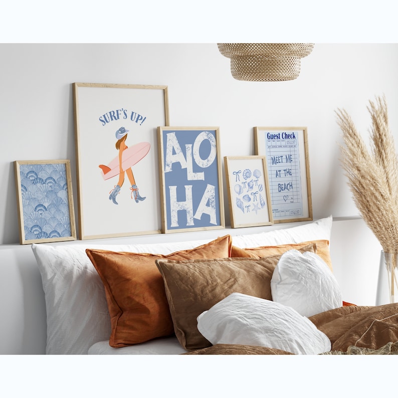 May include: A bedroom with a white bed, brown pillows, and a white blanket. There are five framed prints on the wall above the bed. The prints feature a surfer girl, the word "ALOHA", seashells, and a guest check with the text "Meet me at the beach".