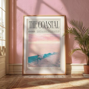 May include: A framed art print titled "THE COASTAL" featuring a serene ocean scene with a surfer riding a wave. The print has a gold frame and is displayed against a pink wall. The text "03/2025" is visible.