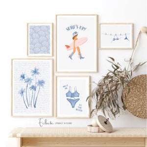 May include: A set of five framed prints with a beach theme. The prints feature a surfer girl, palm trees, seashells, a bikini, and the text "Surf's Up!" and "Meet Me At The Beach".