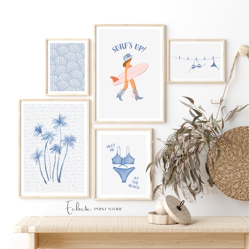 May include: A set of five framed prints with a beach theme. The prints feature a surfer girl, palm trees, seashells, a bikini, and the text "Surf's Up!" and "Meet Me At The Beach".