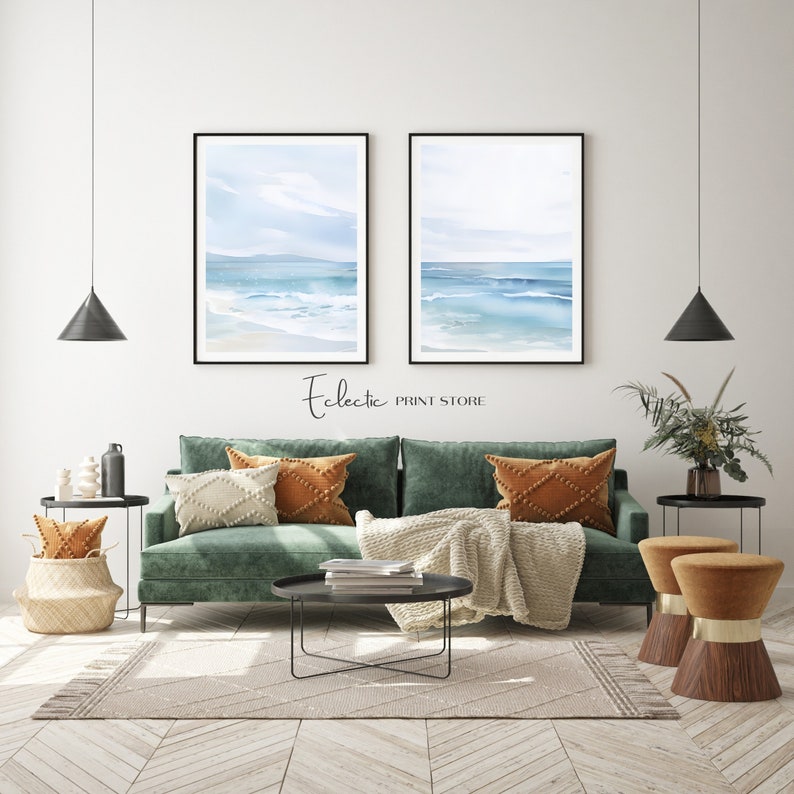 May include: Two watercolor paintings of a seascape with blue water and white waves. The paintings are framed in black and hung on a white wall above a green sofa with throw pillows and a blanket. The sofa is in a living room with a coffee table, two side tables, and a potted plant.