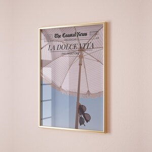 May include: A framed print of a newspaper with the headline "LA DOLCE VITA" and the subheading "THE SWEET LIFE". The image shows a striped beach umbrella and sunglasses hanging from the umbrella.