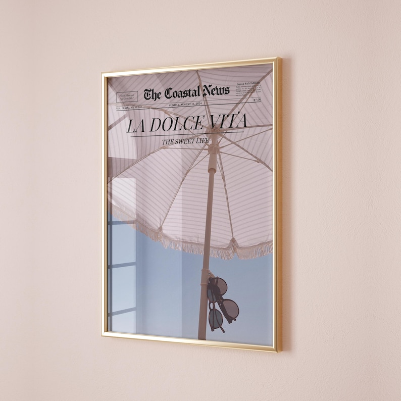 May include: A framed print of a newspaper with the headline "LA DOLCE VITA" and the subheading "THE SWEET LIFE". The image shows a striped beach umbrella and sunglasses hanging from the umbrella.