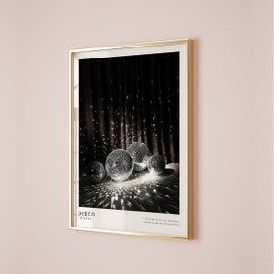May include: A framed poster featuring a black and white photograph of disco balls against a dark backdrop. The poster displays the word "DISCO" in bold white lettering and the text "/ˈdɪskoʊ/" in smaller white lettering. The poster also includes the text "1. the place to be your weird self 2. where we dance the blues away".